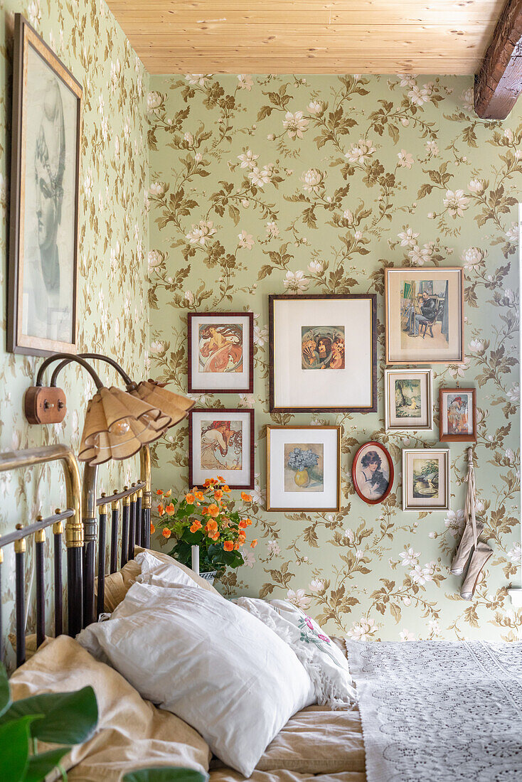 View over bed to gallery of photos on wall with floral wallpaper