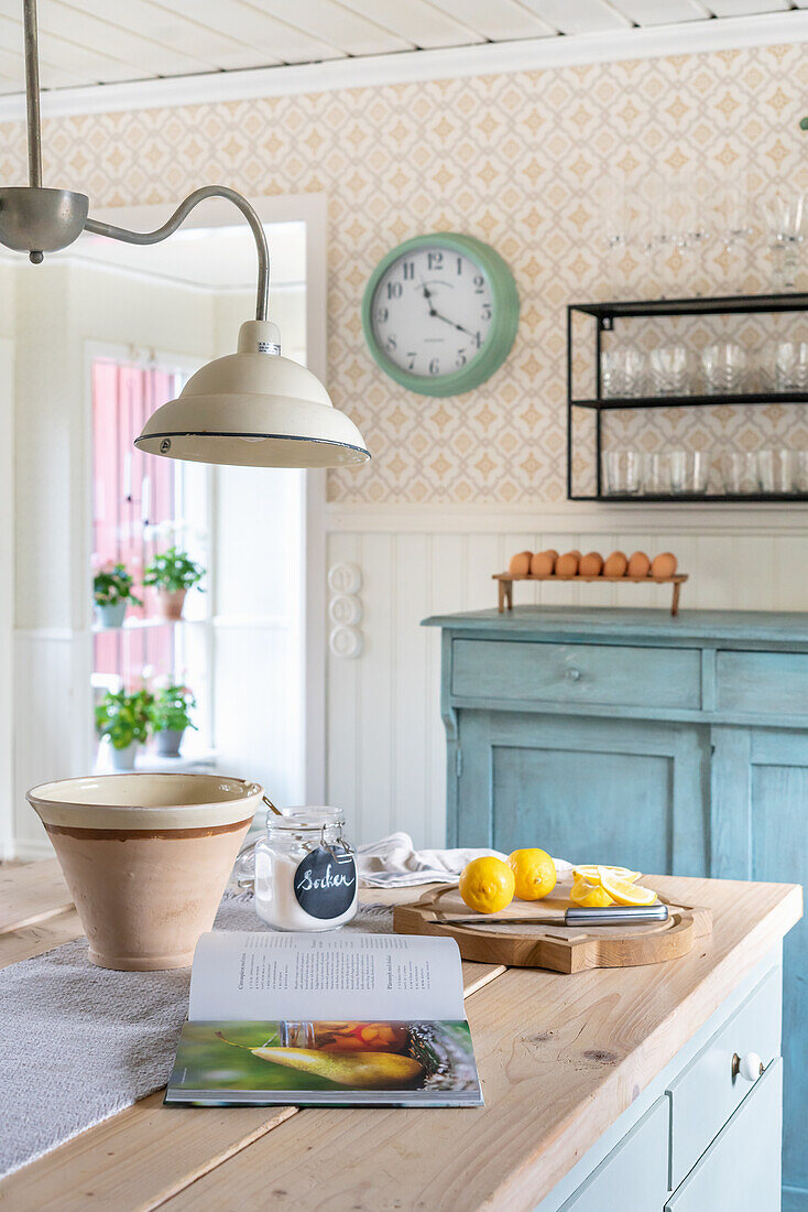 Kücheninsel mit Holzarbeitsplatte, Anrichte, Gläserregal und Wanduhr in nostalgischer Küche