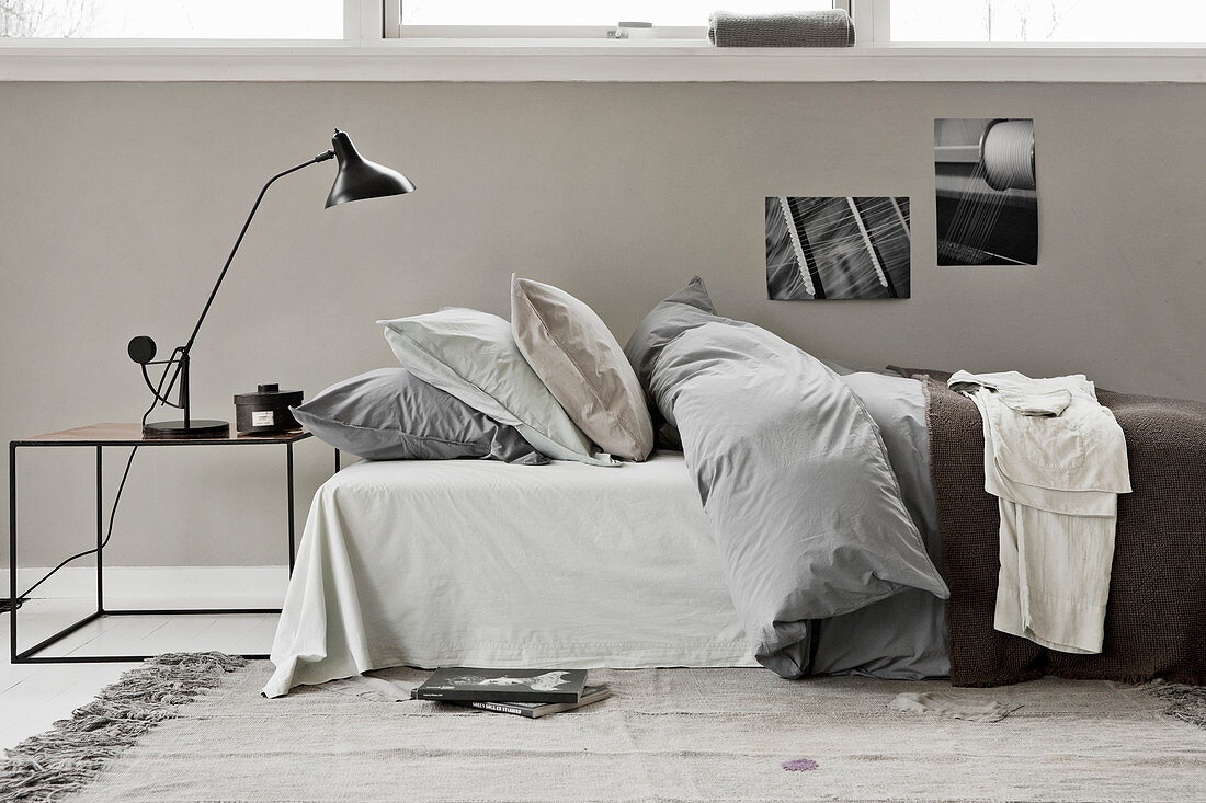 A bed with a duvet and pillows and a bedside table with a reading lamp