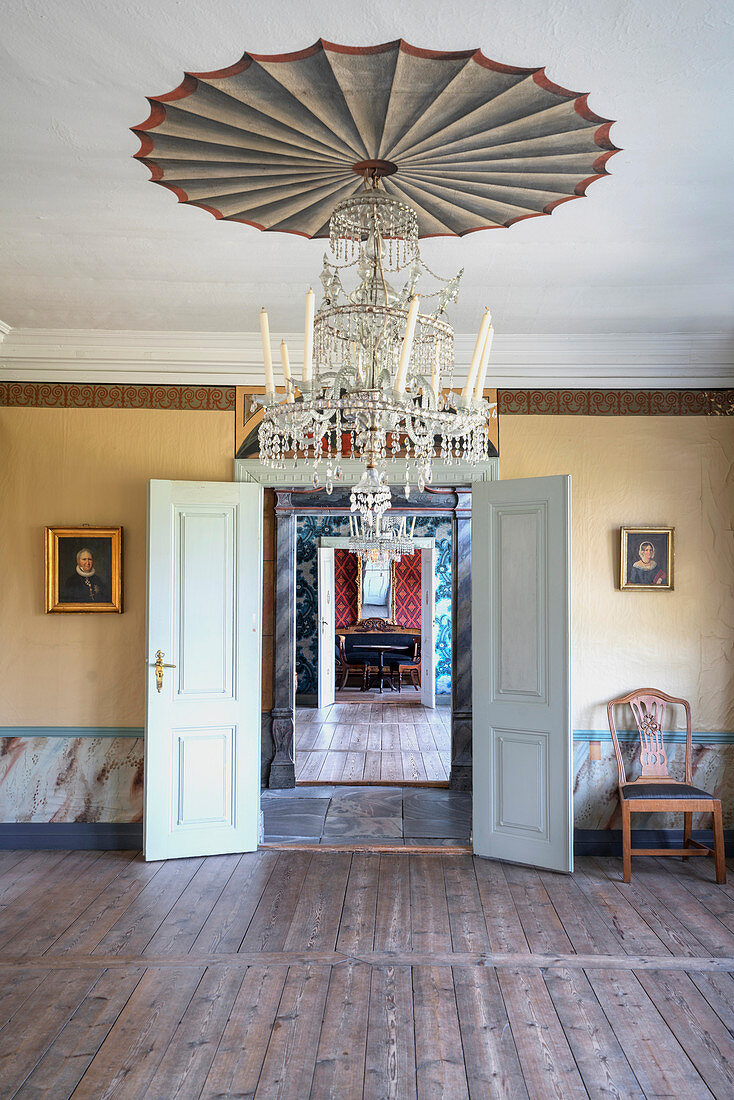 A room with wooden floorboards, a chandelier and portrait paintings