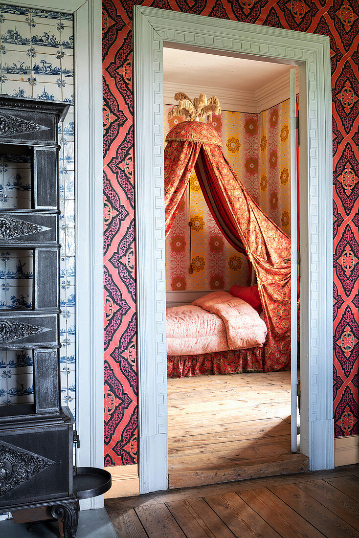 A view into a bedroom with a four-poster bed and wallpaper