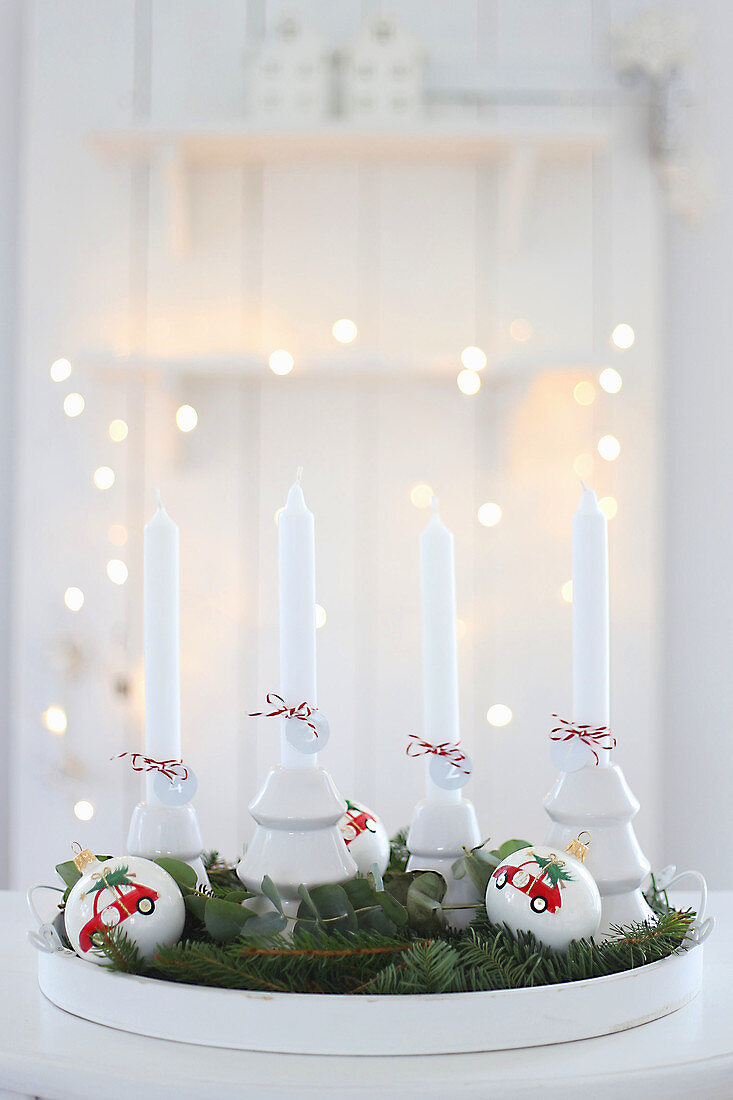 Tablett mit vier weißen Kerzen, Weihnachtskugeln und Tannenzweigen