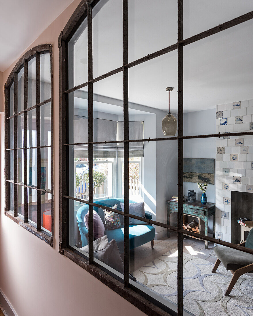 Large french metal salvaged windows with view through to sitting room, tiles around the fireplace, rug and sofa upholstered