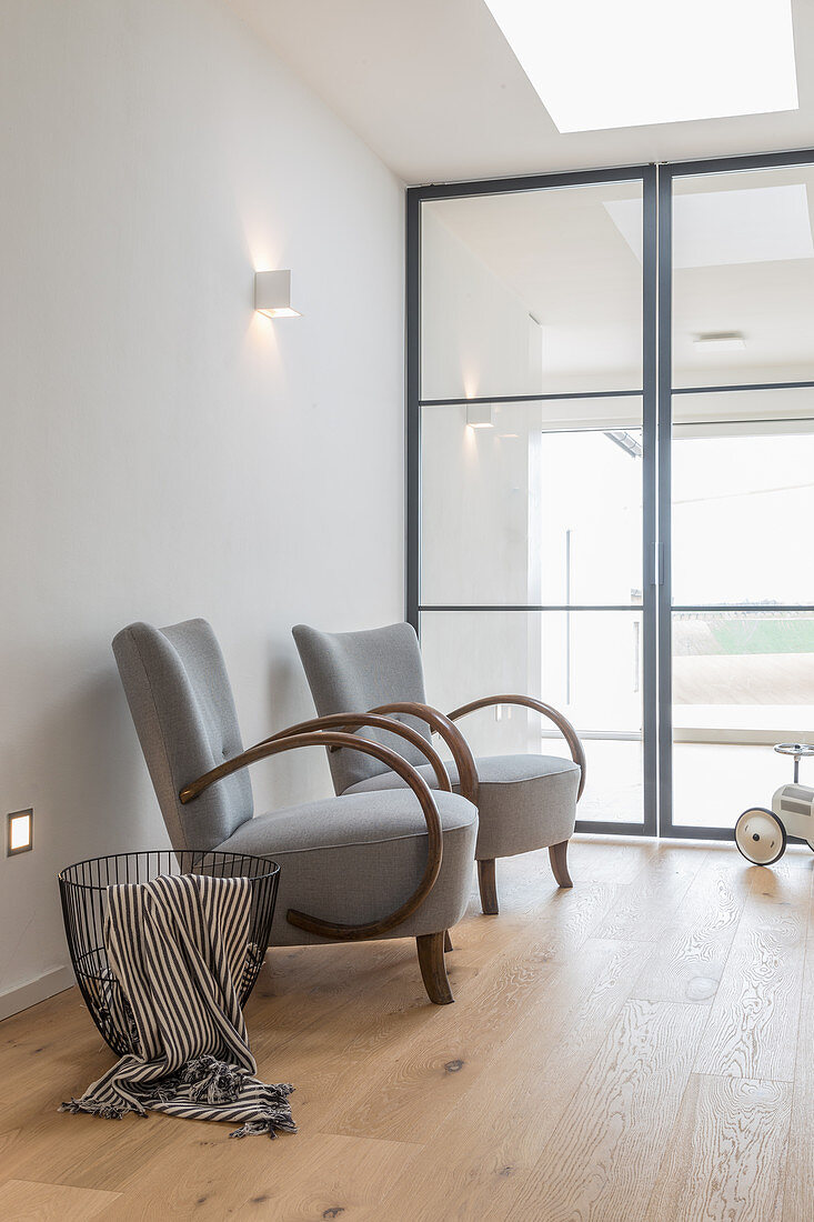 Zwei Sessel und Metallkorb vor verglaster Industrietüren in Loft-Wohnung