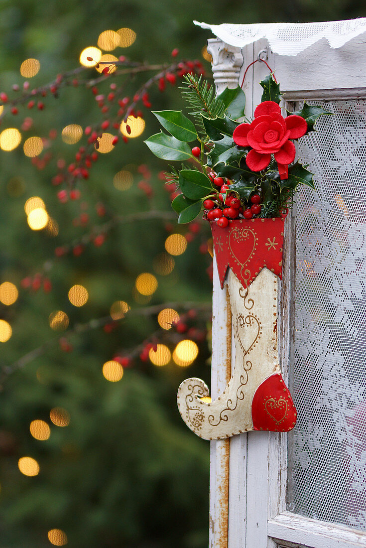 A Christmas stocking filled with red berries and leaves hanging on a window