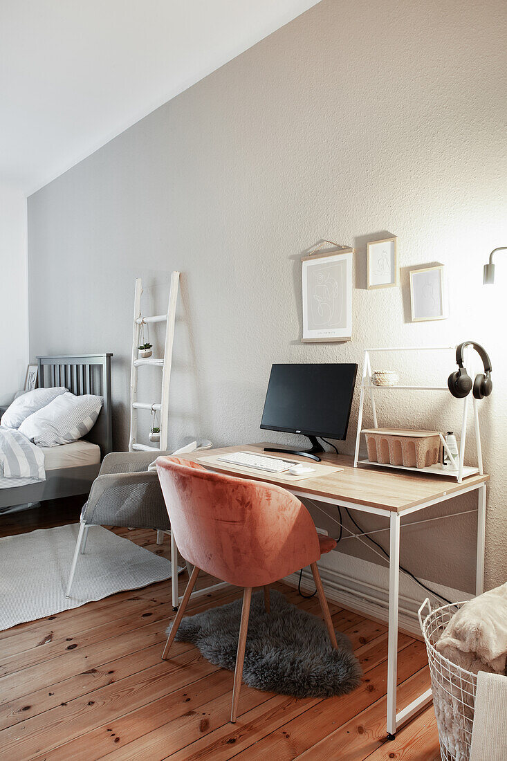 Multifunctional room: desk and shell chair against grey wall with bed in the background