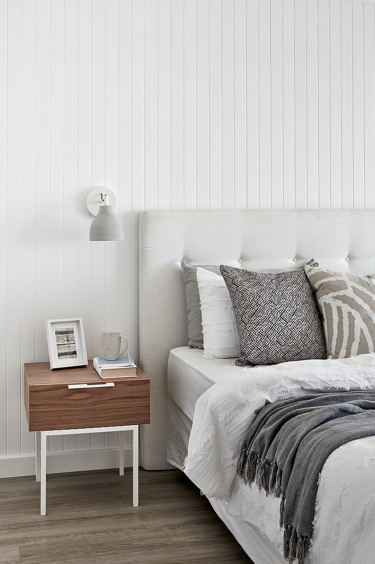 Bett und Nachttisch im Schlafzimmer mit weißer Wandverkleidung