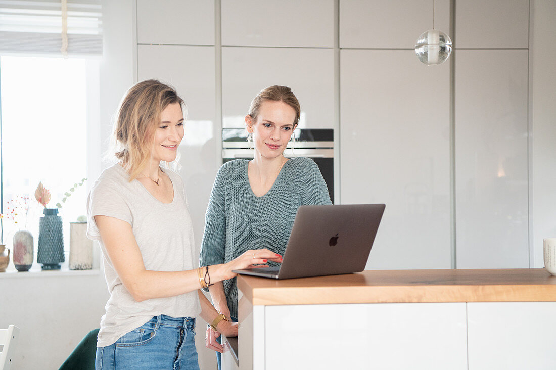Zwei Freundinnen stehen mit Laptop an Küchentheke