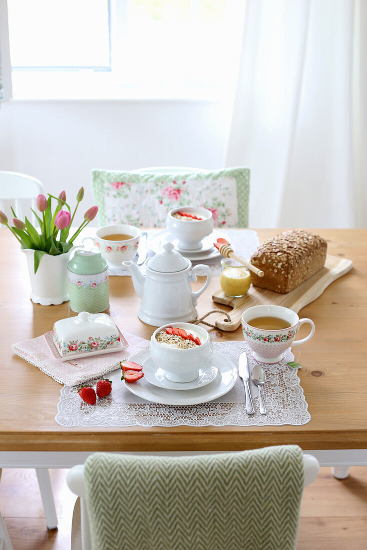Breakfast table set with muesli, tea, loaf of bread and tulips