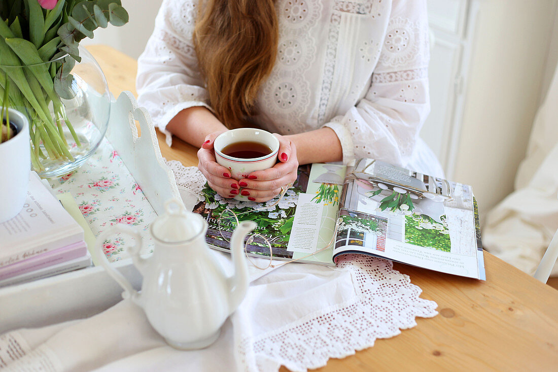 Teekane, Zeitschrift und Frauenhand mit Tee