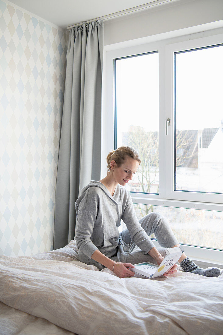 Blonde woman in casual wear sitting on bed with gift