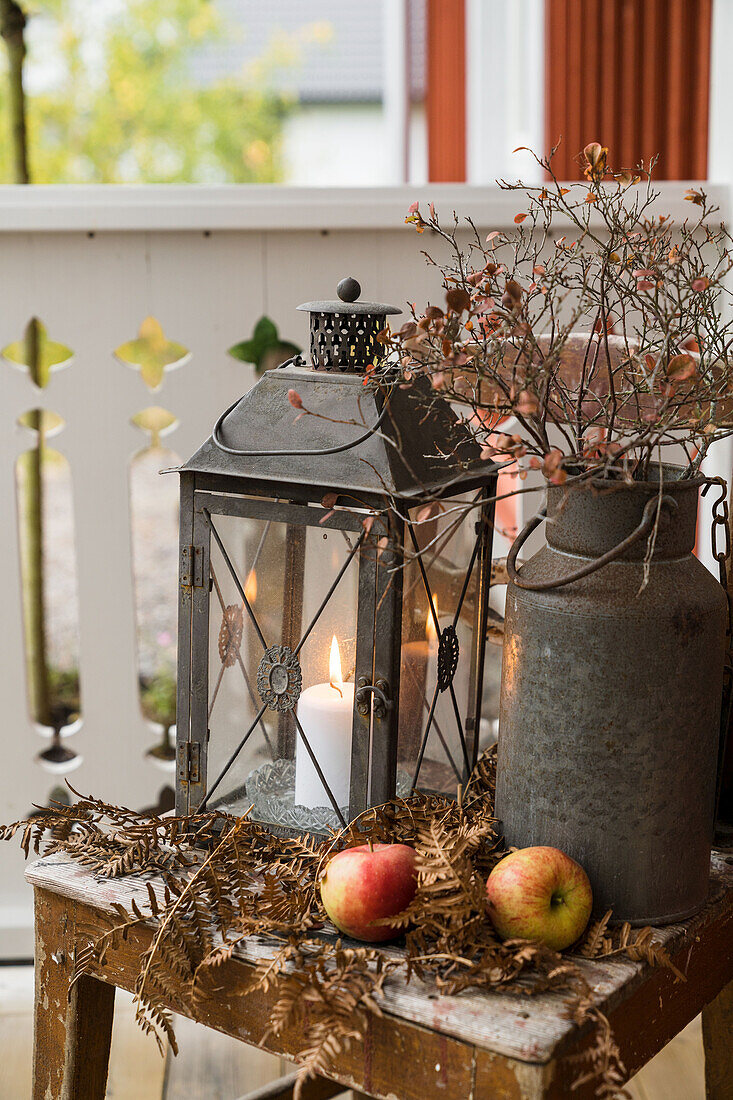 Vintage milk can with dried branches and lantern on a wooden chair