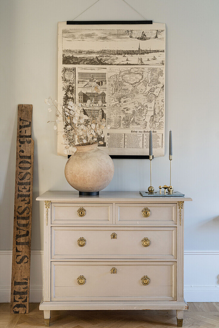 Old poster with a map above chest of drawers with vase and candle holder