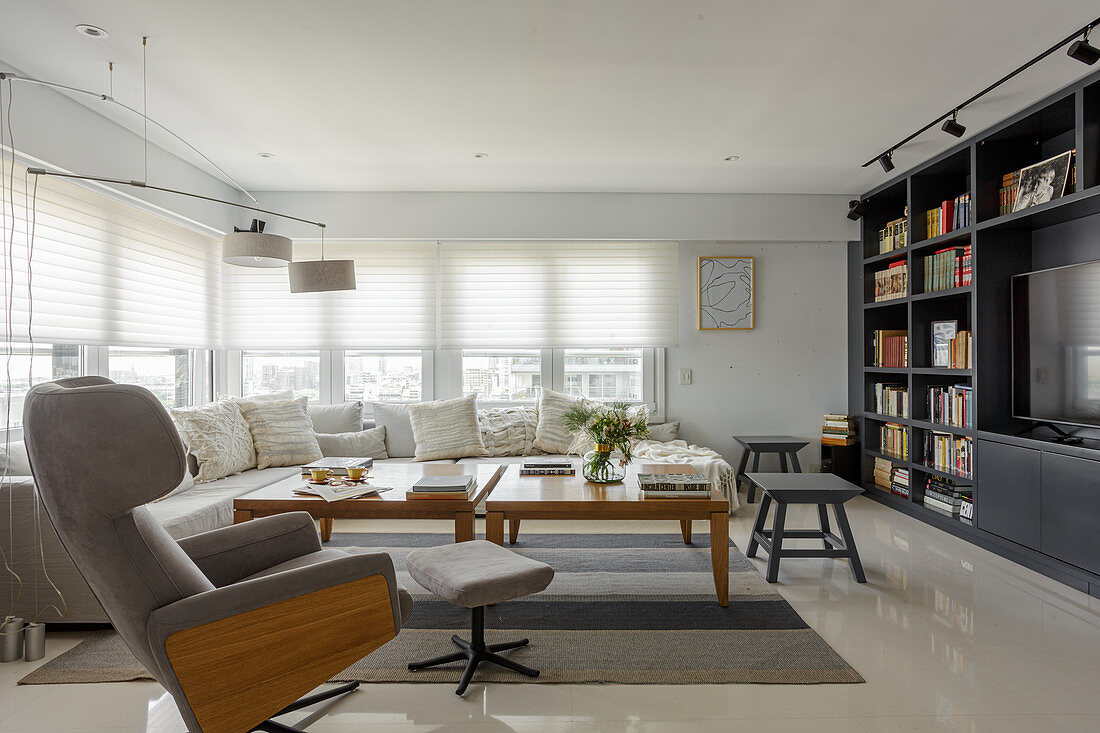 Bequemer Sessel mit Fußschemel, Sofa und Tische vor Wohnzimmerwand mit Bücherregal und TV