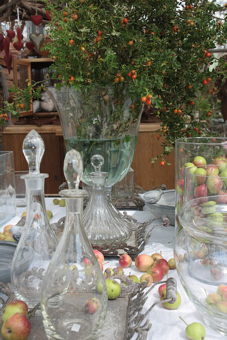 Herbstdekoration mit Glaskaraffen, Äpfeln und Strauß aus Rosenzweigen mit Hagebutten