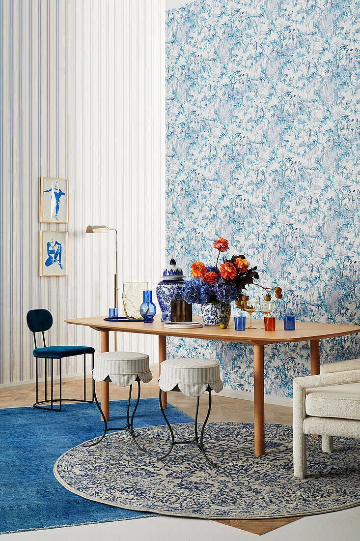 Vase of flowers on table and various seating in front of wall with blue and white wallpaper