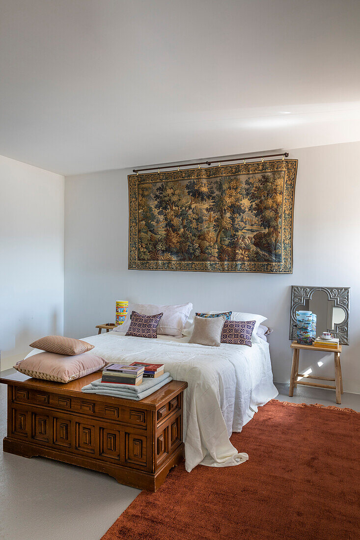 Wandteppich über Doppelbett und antike Holztruhe im Schlafzimmer