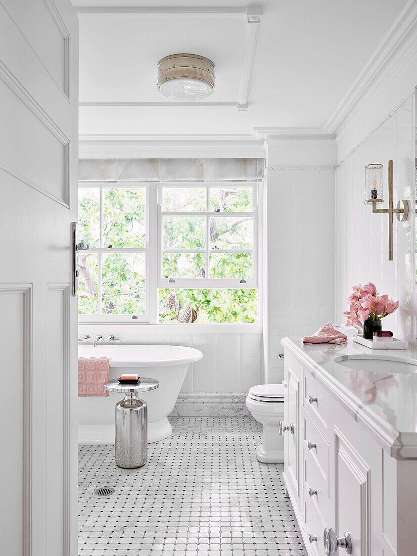 View into white bathroom with vanity and bathtub under the window