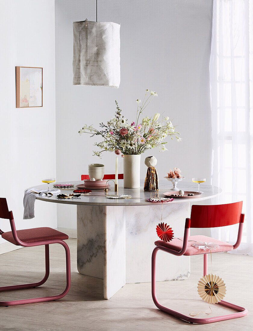 Rote Stühle um Marmortisch mit Blumenstrauß und Weihnachtsdekoration, darüber Hängelampe