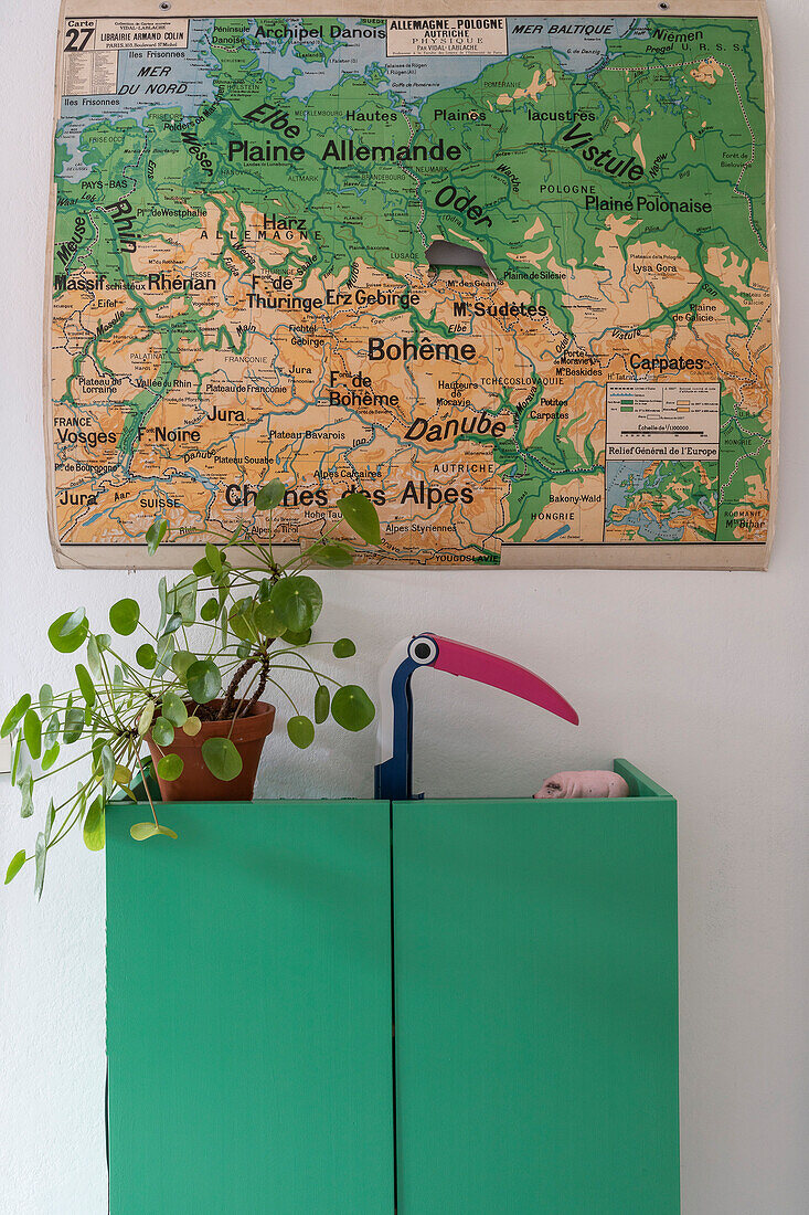 Grüner Schrank mit Zimmerpflanze und Tischleuchte, darüber Landkarte