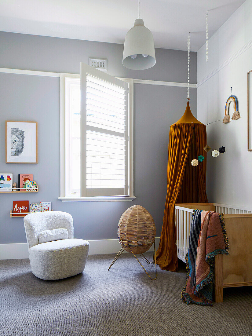 Weißer Sessel, Stehlampe und Babybett mit Baldachin im Zimmer mit grauer Wand