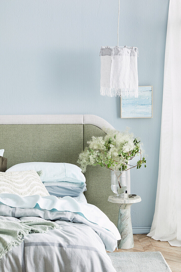 Bed with upholstered headboard, bedside table with bouquet of flowers, above pendant lamp