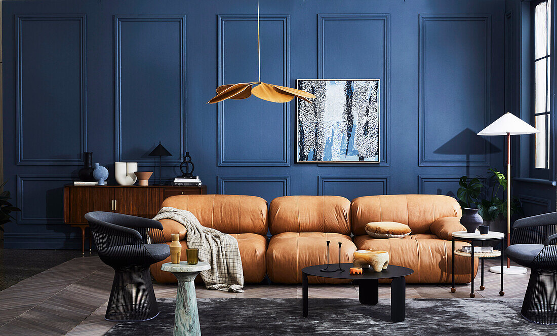 Hellbraunes Ledersofa, schwarze Stühle und Coffeetable im Zimmer mit blauer Wand