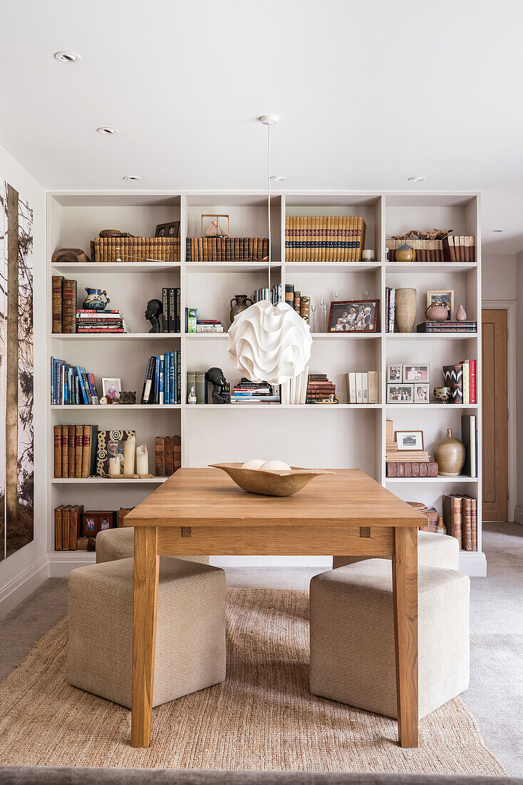 An oak table, cube seats, a paper pendant lamp and a shelf in an open-plan dining room