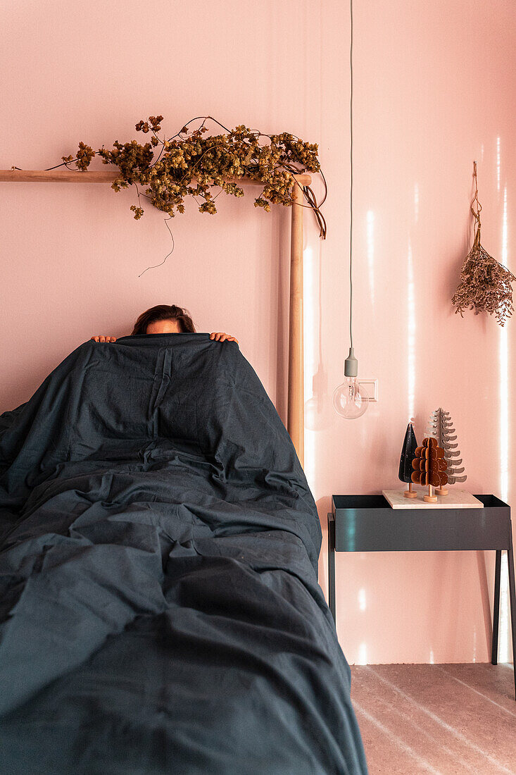 Man hiding under black bedspread in a bohemian style bedroom