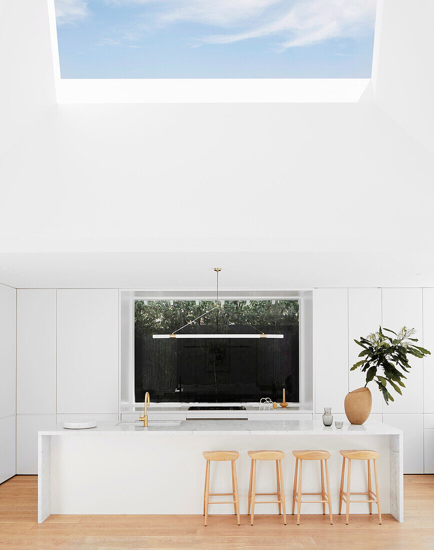 Elegante Kücheninsel mit Marmorplatte und Barhockern in weißer Küche mit Oberlicht