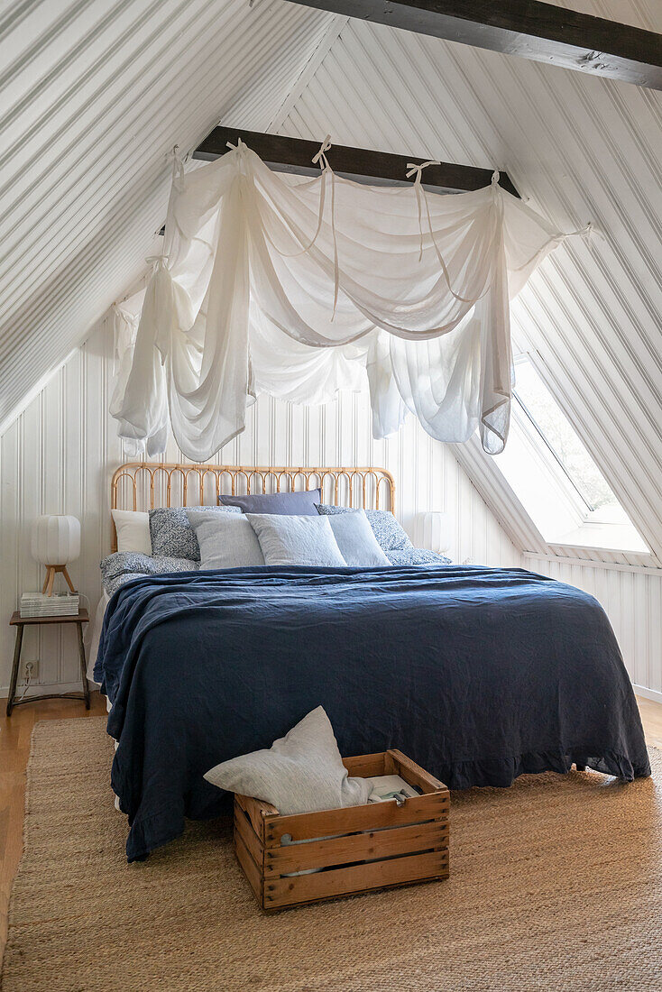 Sommerliches Schlafzimmer mit Moskitonetz unter dem Dach