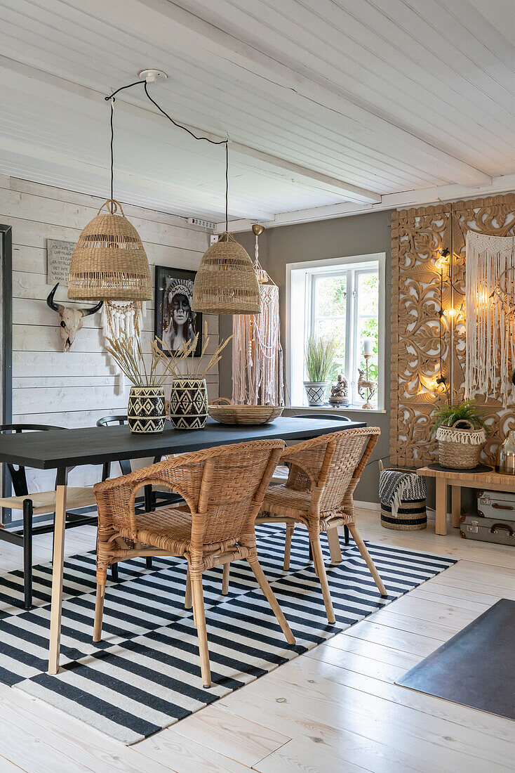 Dining table with rattan armchairs on black and white carpet, above boho hanging pendant light