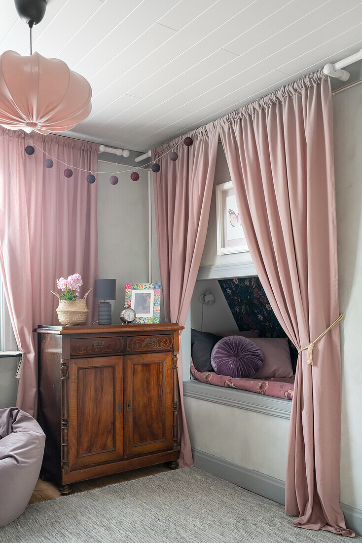 Eingebautes Bett und antiker Schrank im Mädchenzimmer mit hellgrauen Wänden und rosafarbenen, bodenlangen Vorhängen