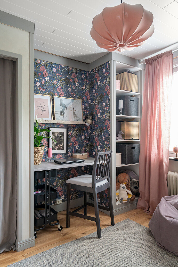 Desk in girl's bedroom with floral wallpaper, built-in shelves and pink curtains