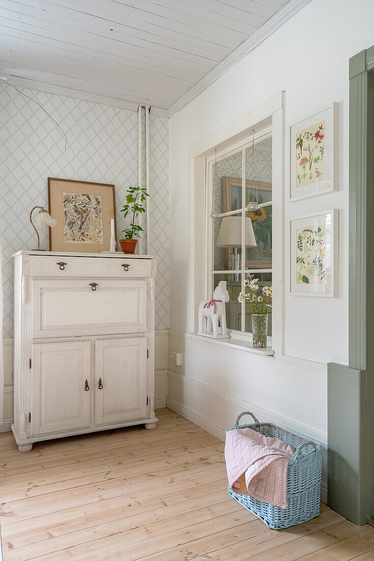 Old, white-painted bureau next to interior window in room with wooden floorboards