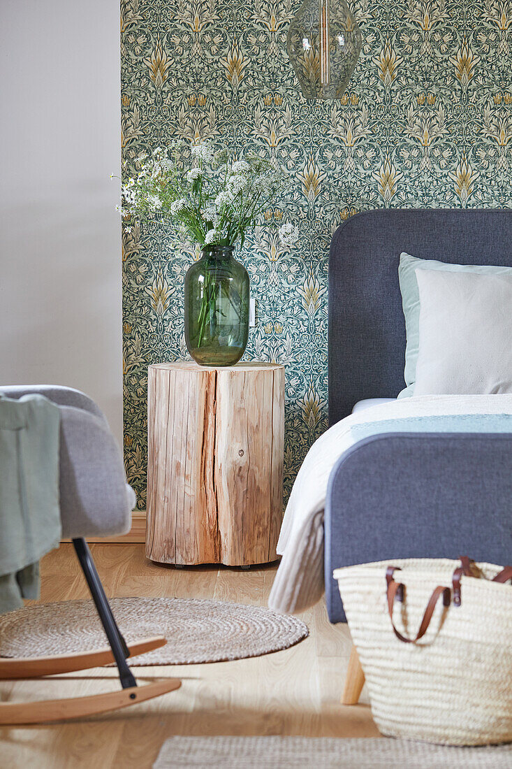 Baumstamm-Nachttisch neben Doppelbett vor tapezierter Wand im Schlafzimmer