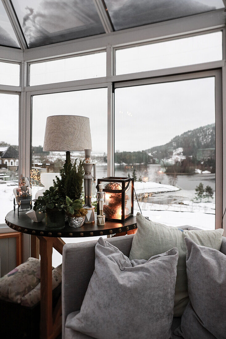 Weihnachtlich dekorierter runder Tisch neben Sofa mit Kissen am Fenster