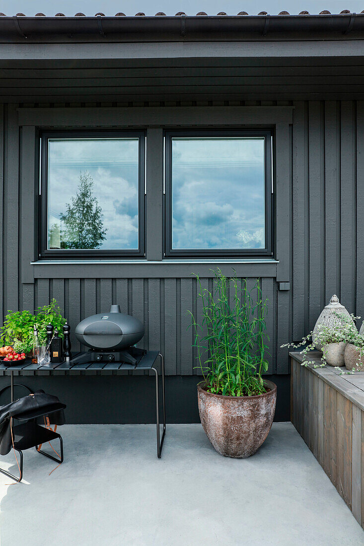 Small modern barbecue on grey bench against anthracite-coloured façade