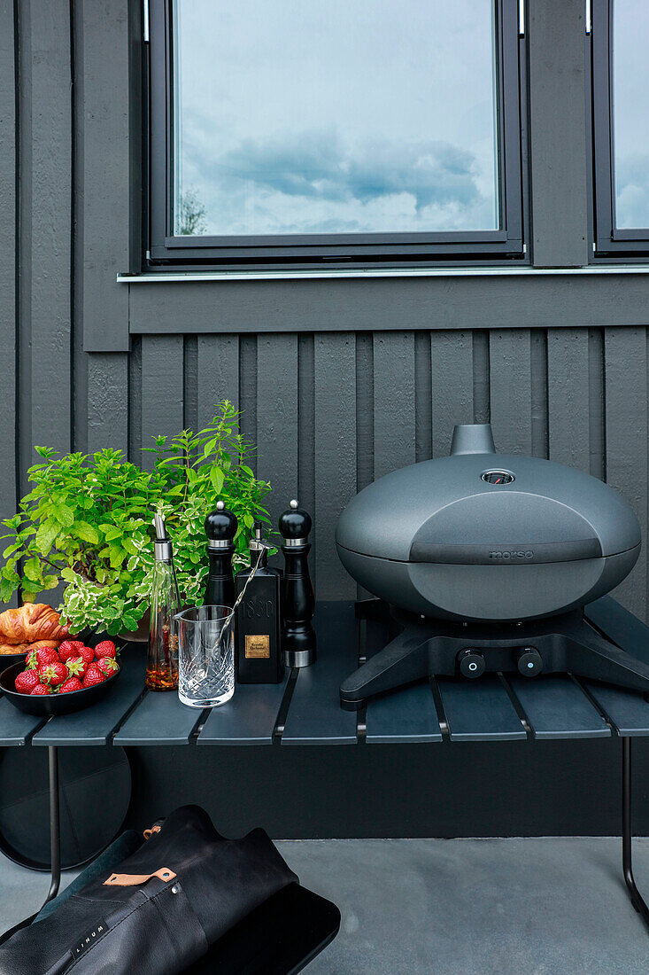 Small modern barbecue on grey bench in front of anthracite-coloured facade