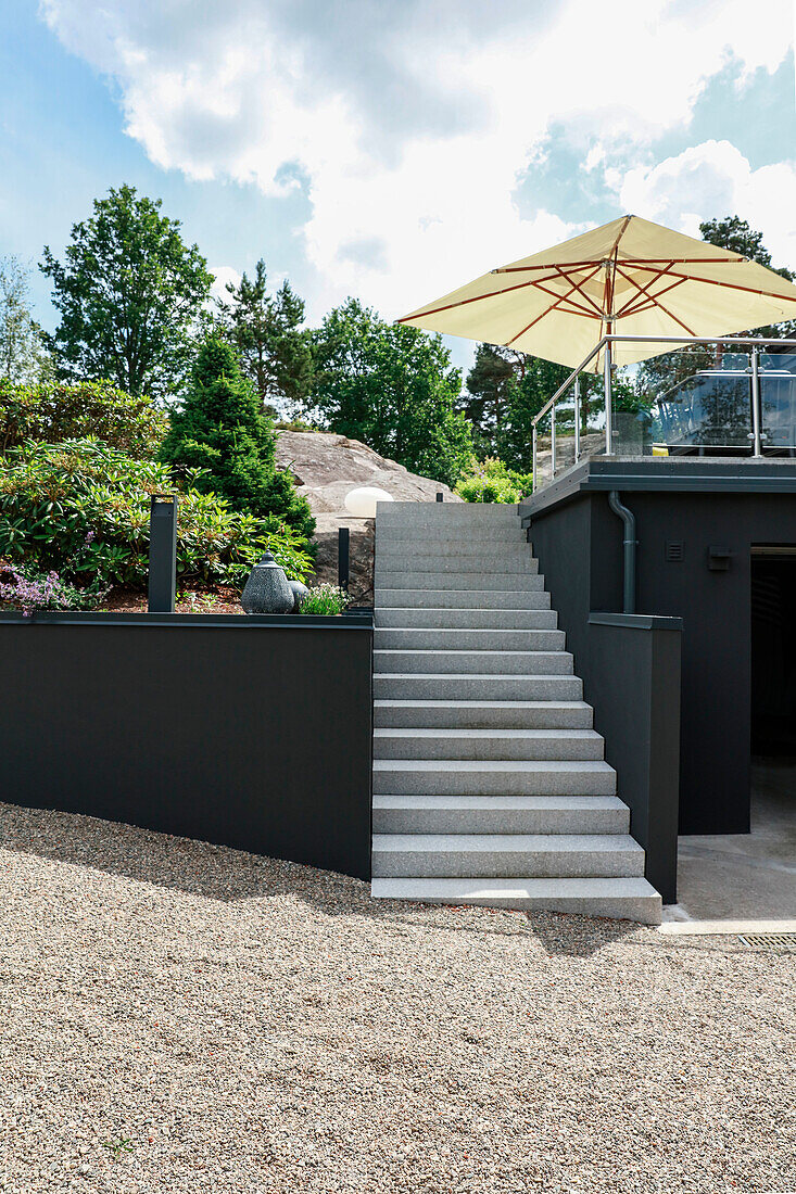 Stairs leading to a modern garden with grey walls and roof terrace on top of the garage