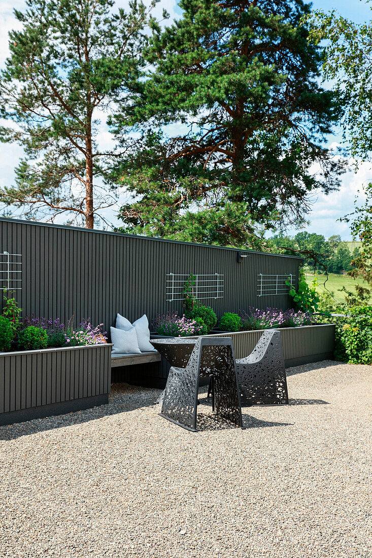 Modern garden chairs in front of a bench between two raised beds against a screen wall in grey