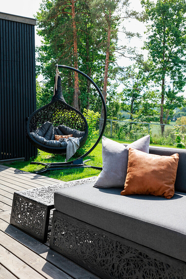 Modern outdoor lounge and hanging chair in dark grey in summer garden