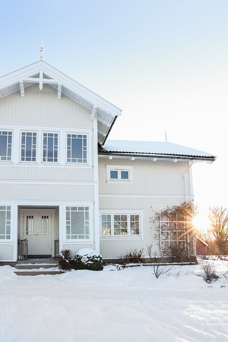 Weißes, zweigeschossiges Holzhaus mit schneebedecktem Garten