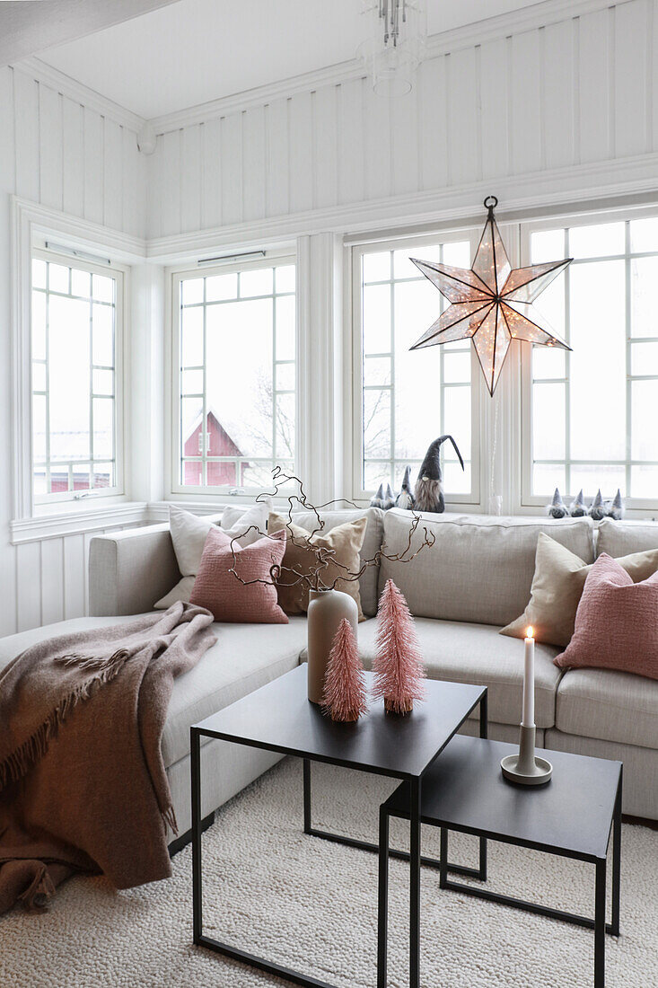 Couchtisch, hellgraue Sofagarnitur mit Kissen und weihnachtlich dekoriertes Fenster im Wohnzimmer