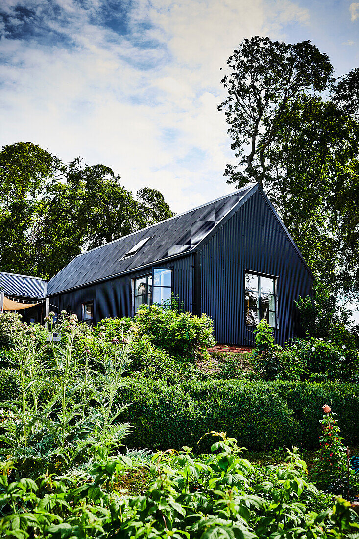 Haus mit schwarzem Wellblech verkleidet in sommerlichem Garten