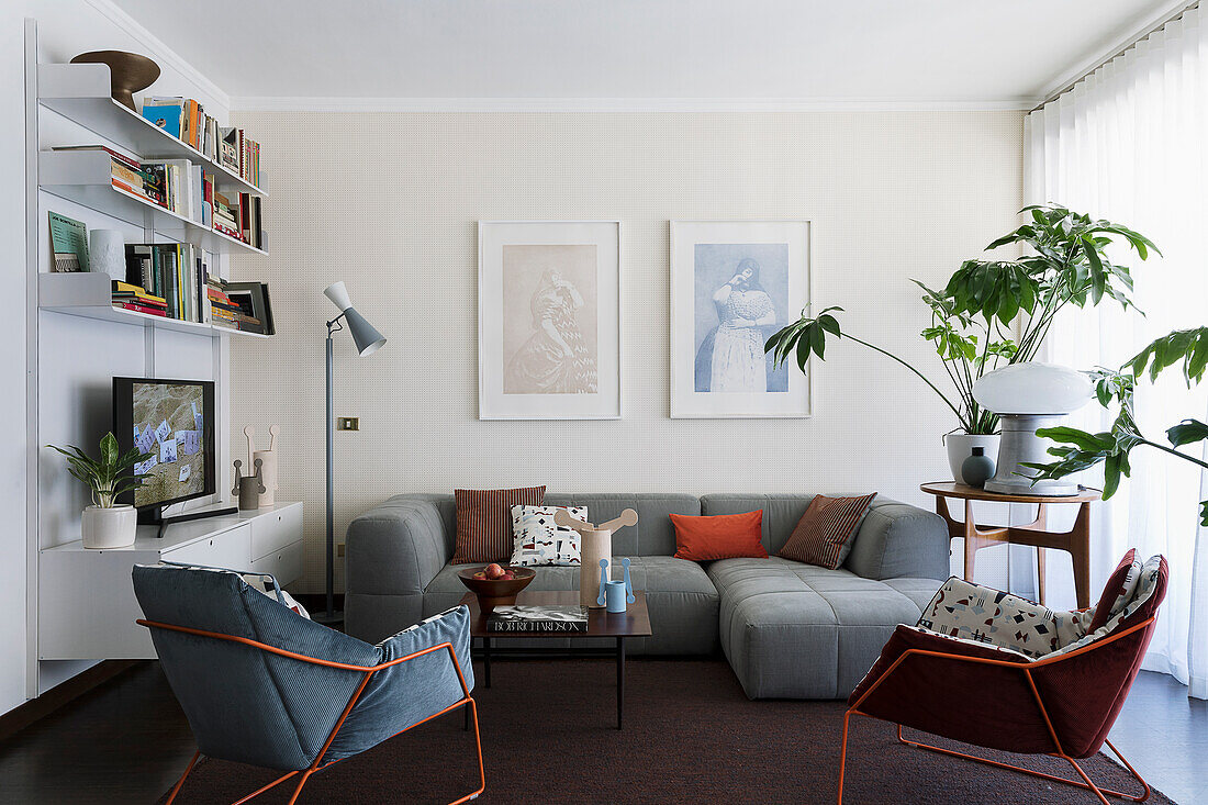 Graue Sofagarnitur und Sessel mit Metallstruktur, Zimmerpflanzen und Regale im Wohnzimmer mit dunklem Boden