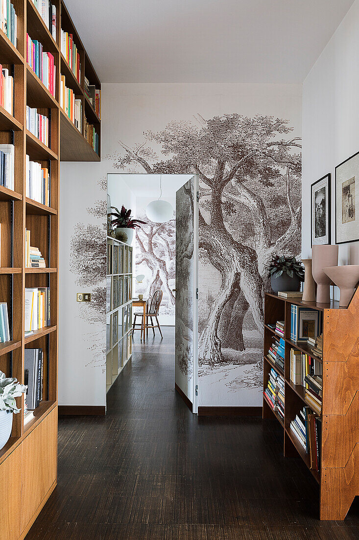 Raumhohes Bücherregal und Tapete mit Baummotiv auf dem Flur mit geöffneter Zimmertür