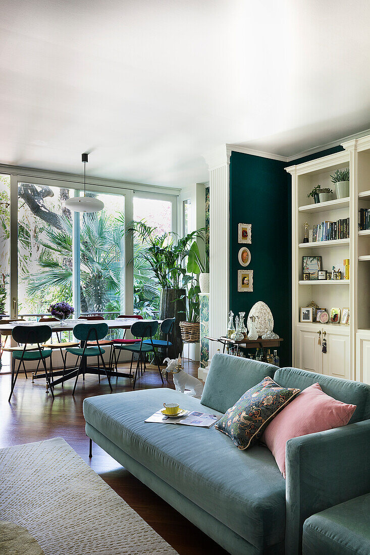 Green sofa in open-plan interior with dining area next to glass wall in background