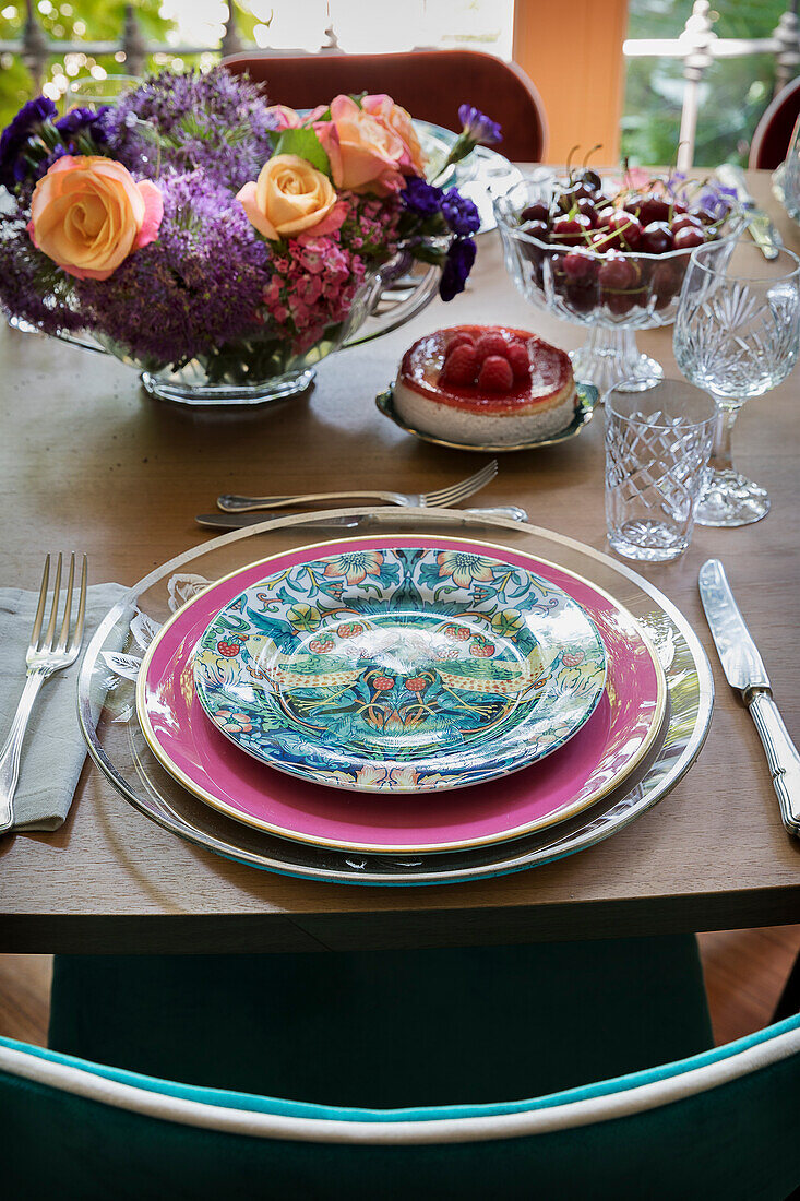 Festively set dining table with colourful plates, crystal glasses and bouquet of flowers
