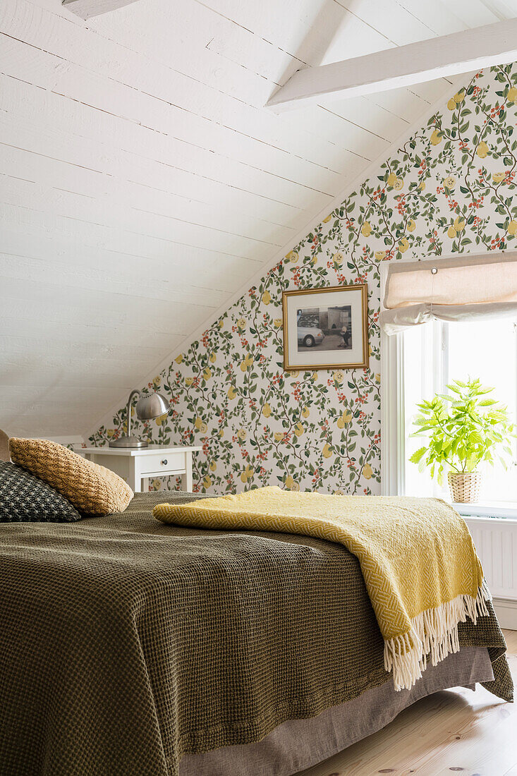 Double bed in bedroom with floral wallpaper and wood-panelled sloping ceiling